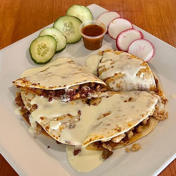 Three cheesy quesadillas with meat filling, served with sliced cucumbers, radishes, and a side of sauce.