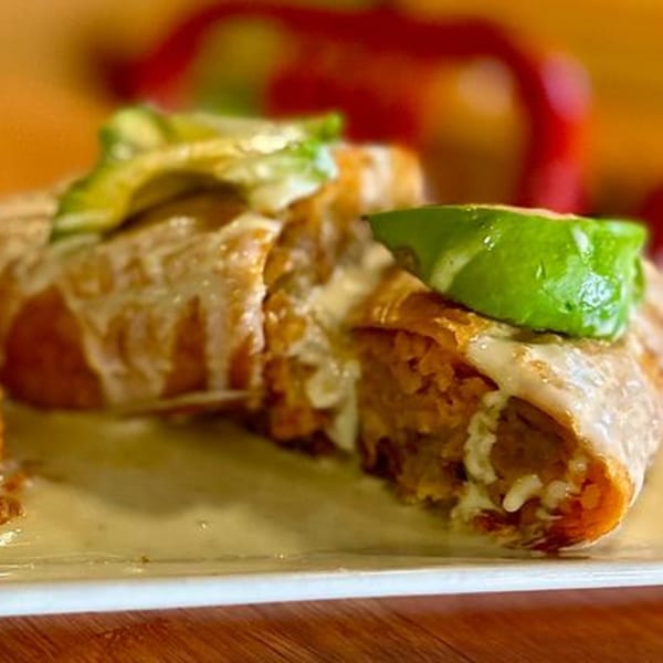 A close-up of a Taco-Holics Club burrito, topped with white sauce and avocado slices.