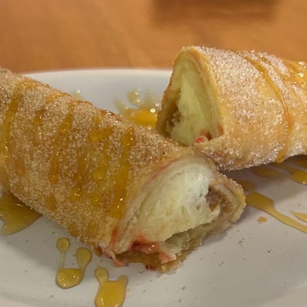 Two churro-like desserts, one cut in half, revealing a creamy filling, drizzled with honey.