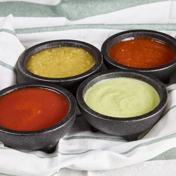 Four bowls of vibrant red and green Mexican salsas are arranged on a striped white cloth.
