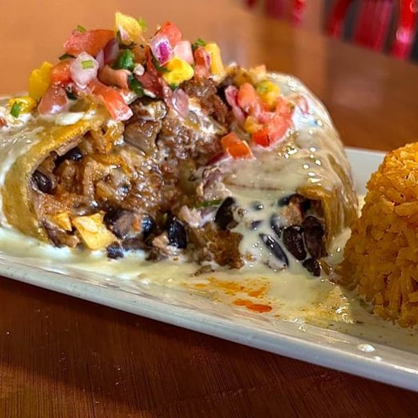 A large, cut burrito filled with meat and beans, topped with pico de gallo and white sauce, served with rice.
